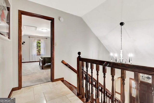 corridor with baseboards, attic access, lofted ceiling, an upstairs landing, and an inviting chandelier