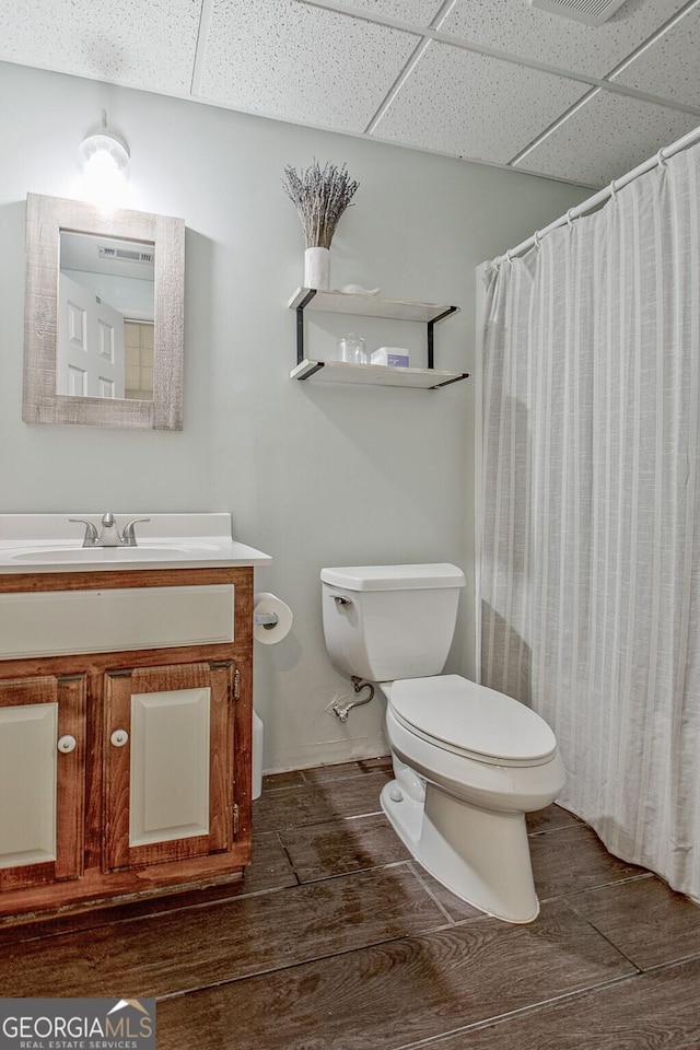 full bath with toilet, a paneled ceiling, and wood finished floors