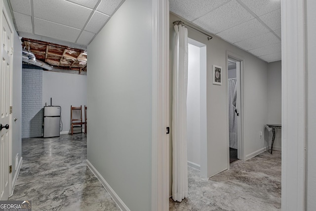 hall with a drop ceiling, baseboards, and concrete flooring