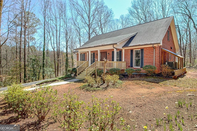 view of front of home featuring brick siding, central AC unit, a porch, and roof with shingles