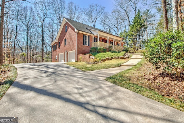 view of side of property with brick siding, covered porch, driveway, and a garage