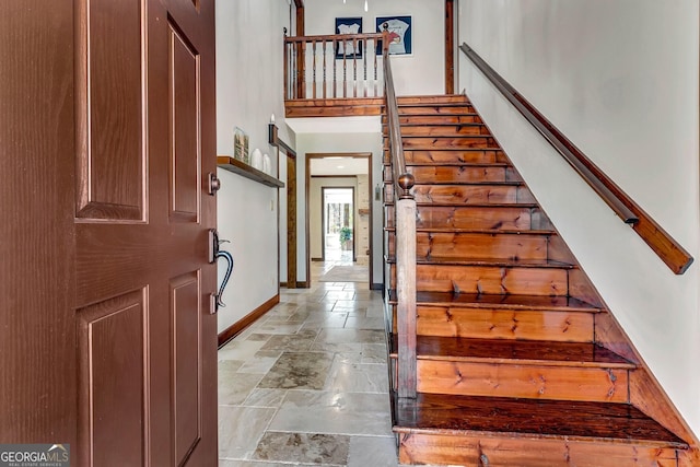 staircase with stone tile floors, a high ceiling, and baseboards