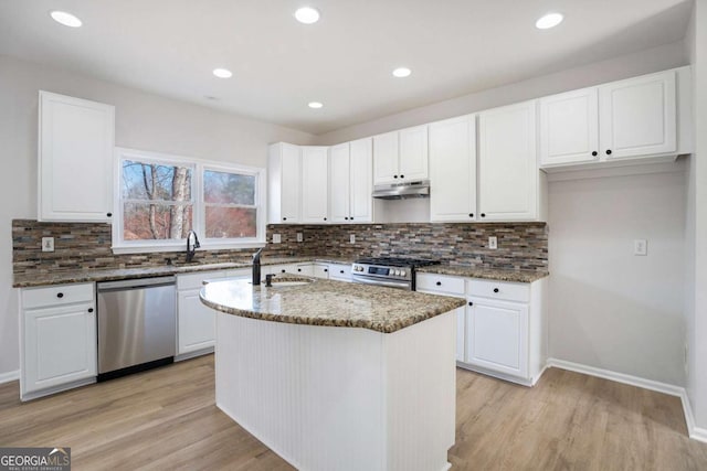 10950 Glenhurst Pass, Duluth, GA 30097 - kitchen with appliances with stainless steel finishes, under cabinet range hood, dark stone counters, a sink, and light wood finished floors