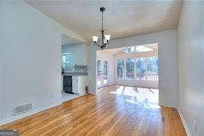 unfurnished living room featuring a notable chandelier, baseboards, visible vents, and wood finished floors