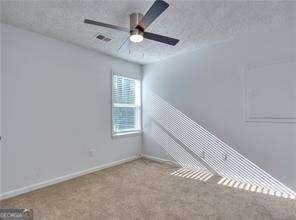 carpeted empty room with visible vents, baseboards, a textured ceiling, and ceiling fan