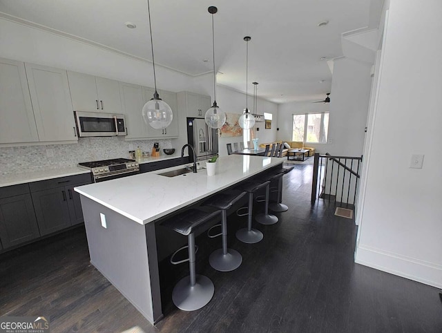 kitchen featuring a spacious island, a sink, stainless steel appliances, dark wood-type flooring, and backsplash