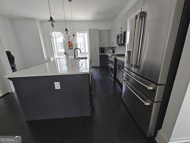 kitchen featuring dark wood-style floors, a center island with sink, stainless steel appliances, decorative light fixtures, and backsplash