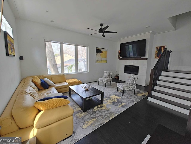 living area with stairs, wood finished floors, a ceiling fan, and a fireplace