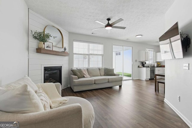 living area featuring a large fireplace, a textured ceiling, dark wood-style flooring, and a ceiling fan