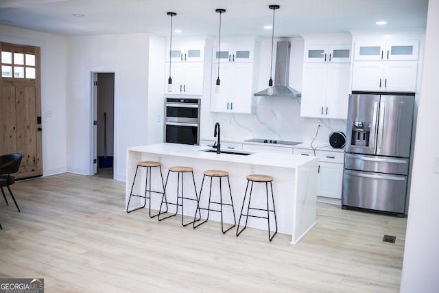 kitchen with wall chimney range hood, a sink, appliances with stainless steel finishes, a kitchen breakfast bar, and backsplash