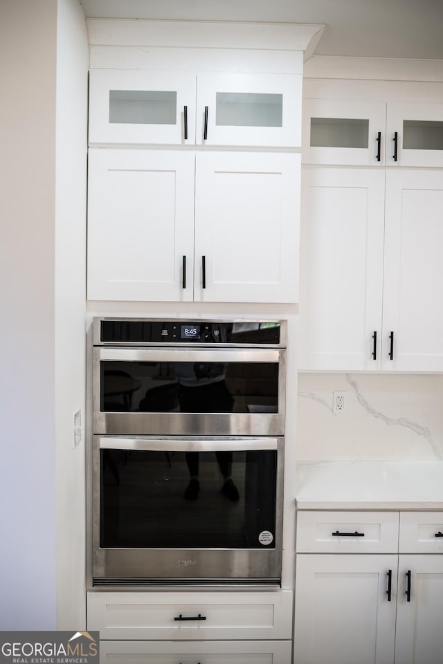 room details with decorative backsplash, stainless steel double oven, white cabinets, light countertops, and glass insert cabinets