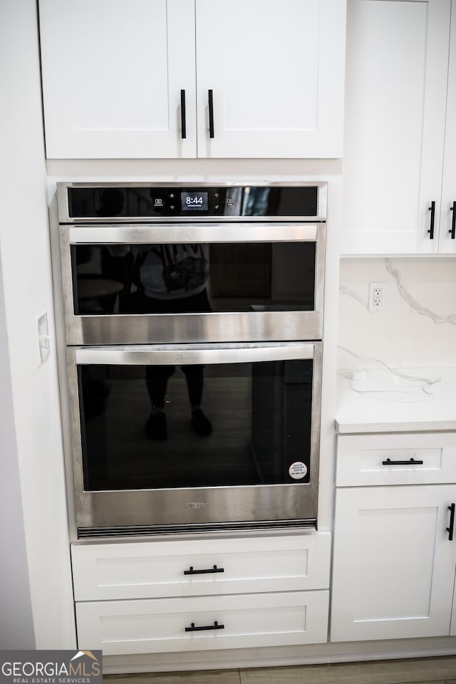 interior details featuring white cabinets, backsplash, and stainless steel double oven