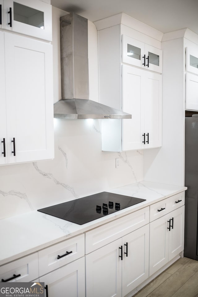 kitchen with wall chimney range hood, white cabinets, black electric stovetop, and backsplash