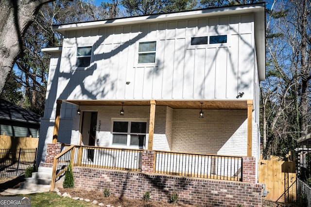 view of front of home featuring covered porch, board and batten siding, brick siding, and fence