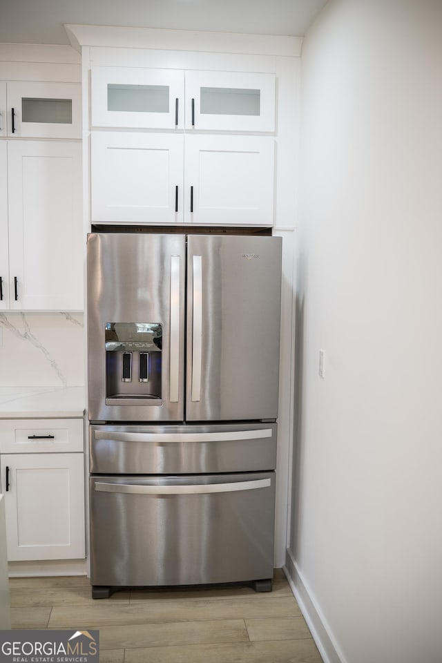 interior details with light wood-type flooring, tasteful backsplash, white cabinetry, stainless steel fridge with ice dispenser, and light countertops