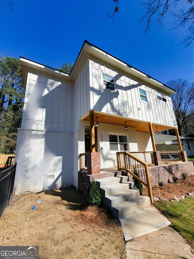 view of front of property featuring brick siding, covered porch, board and batten siding, and fence