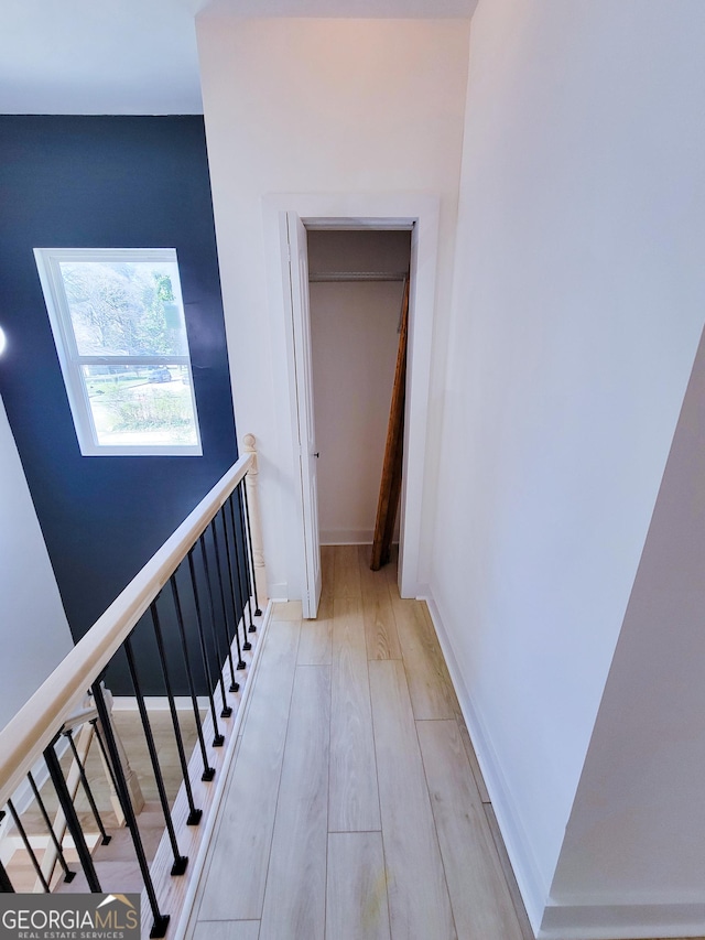 hallway featuring baseboards, an upstairs landing, and light wood finished floors