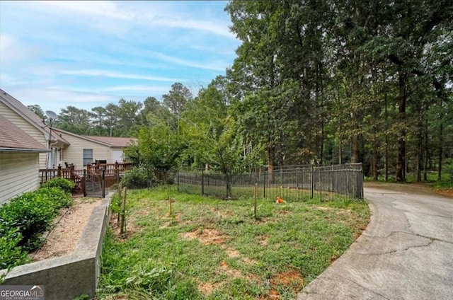 view of yard featuring a wooden deck, concrete driveway, and fence