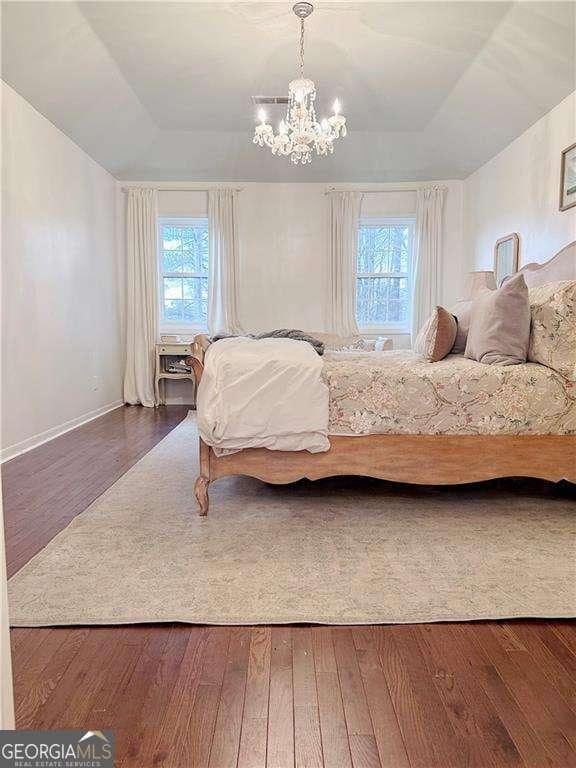 bedroom featuring an inviting chandelier, a tray ceiling, and wood-type flooring