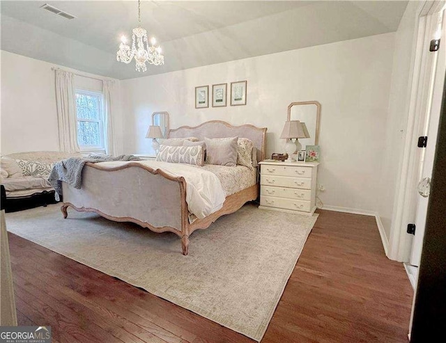 bedroom with visible vents, baseboards, a notable chandelier, and wood finished floors