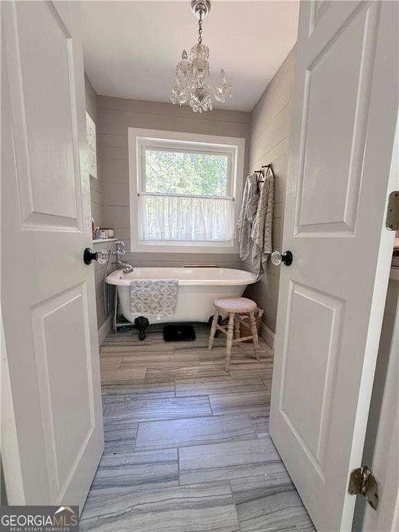 bathroom with a soaking tub, wood finished floors, and a chandelier