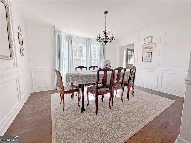 dining area with dark wood finished floors, an inviting chandelier, and a decorative wall