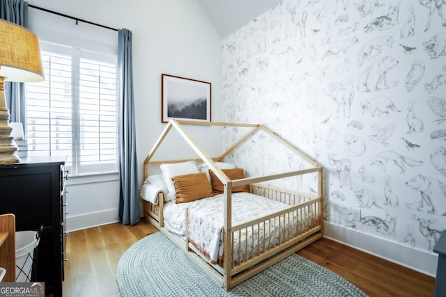 bedroom with baseboards, wallpapered walls, lofted ceiling, and wood finished floors