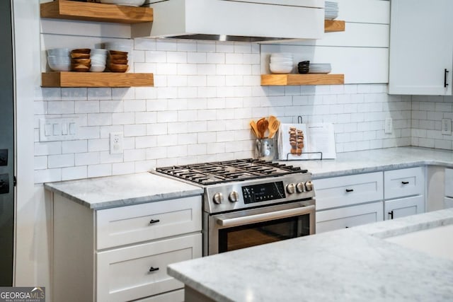 kitchen featuring open shelves, decorative backsplash, stainless steel gas stove, and wall chimney exhaust hood