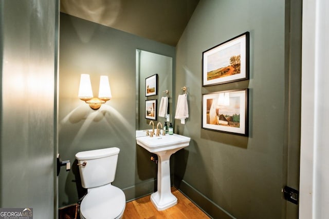 half bathroom with toilet, wood finished floors, and baseboards