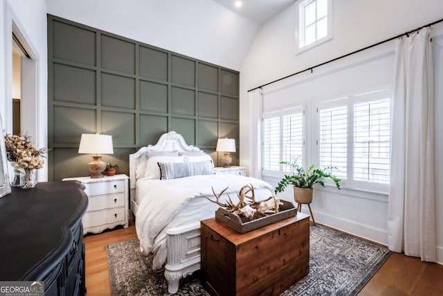 bedroom featuring a decorative wall, multiple windows, lofted ceiling, and wood finished floors