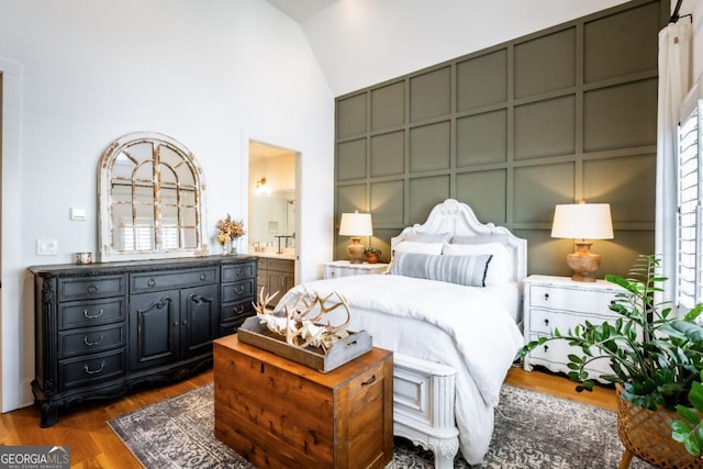 bedroom with dark wood-style floors, a decorative wall, high vaulted ceiling, and ensuite bathroom