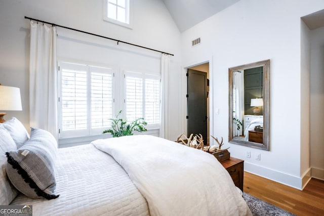 bedroom featuring access to exterior, visible vents, baseboards, wood finished floors, and high vaulted ceiling