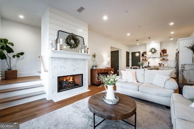 living room with recessed lighting, wood finished floors, visible vents, and a high end fireplace