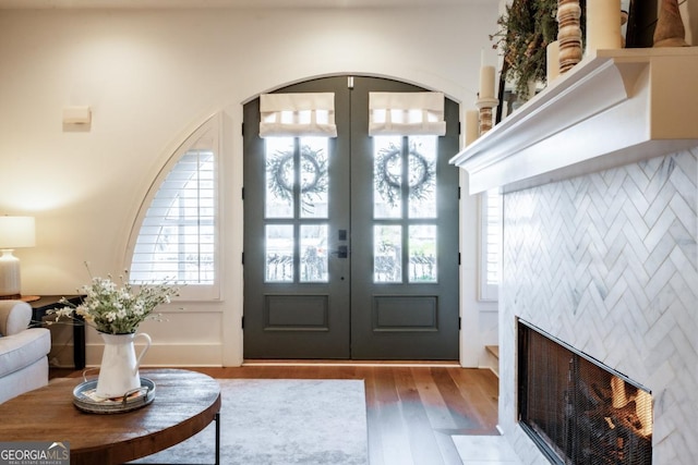 entrance foyer with a fireplace with flush hearth, wood finished floors, arched walkways, and french doors