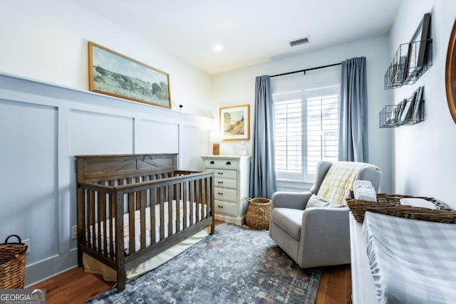 bedroom with visible vents, a crib, wood finished floors, and a decorative wall