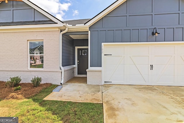 view of exterior entry with a garage, brick siding, board and batten siding, and driveway