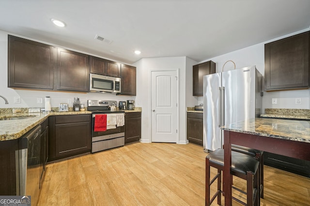 kitchen with visible vents, dark brown cabinetry, light wood-style floors, stainless steel appliances, and a sink