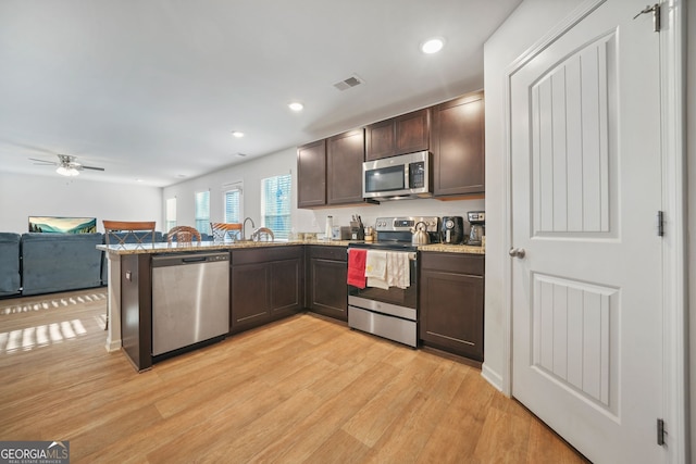 kitchen featuring light wood-style flooring, open floor plan, dark brown cabinetry, appliances with stainless steel finishes, and a peninsula