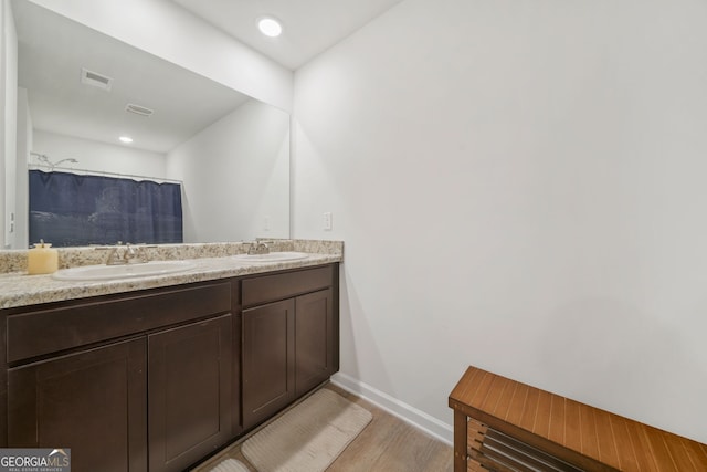 full bath with a sink, visible vents, wood finished floors, and double vanity