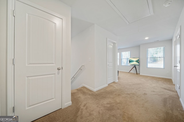 hallway with attic access, an upstairs landing, light colored carpet, and baseboards