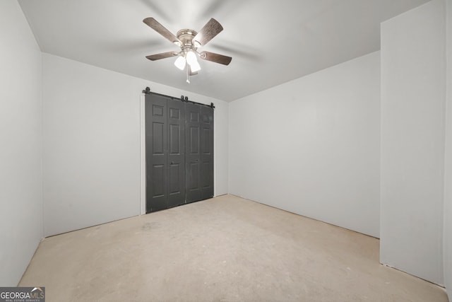 unfurnished bedroom with a barn door, unfinished concrete flooring, a closet, and ceiling fan