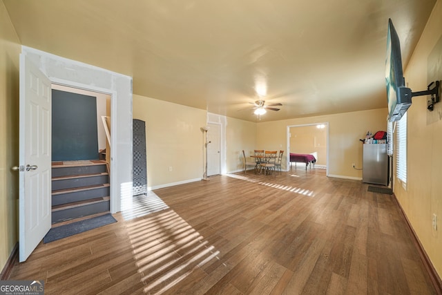 unfurnished living room with wood finished floors, stairway, a ceiling fan, and baseboards