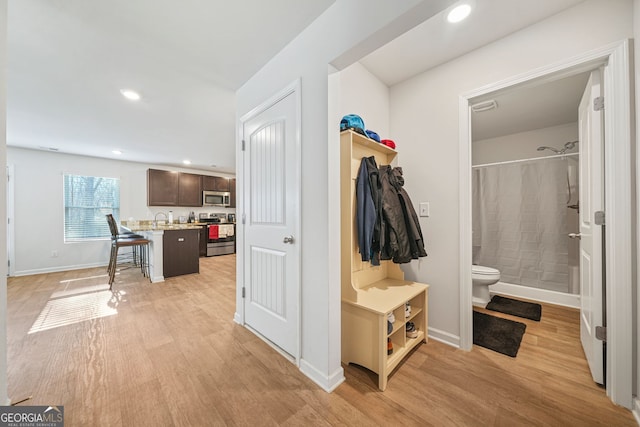 corridor featuring recessed lighting, baseboards, light wood finished floors, and a sink