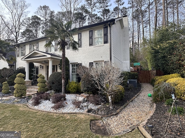 view of front facade featuring cooling unit, brick siding, a chimney, and fence