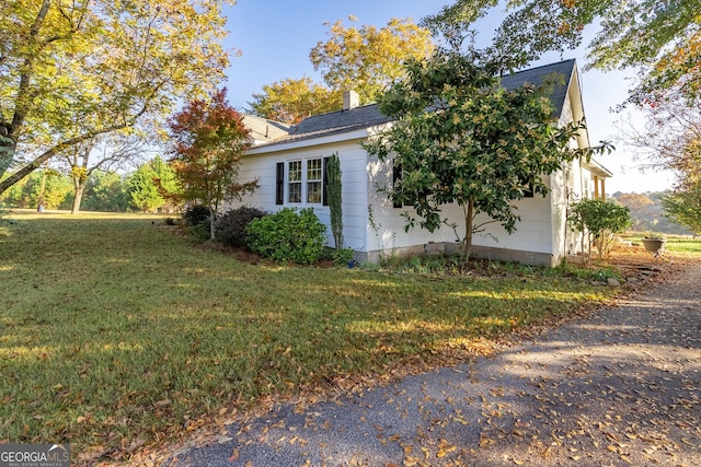 view of property exterior featuring a yard, a garage, roof with shingles, and a chimney