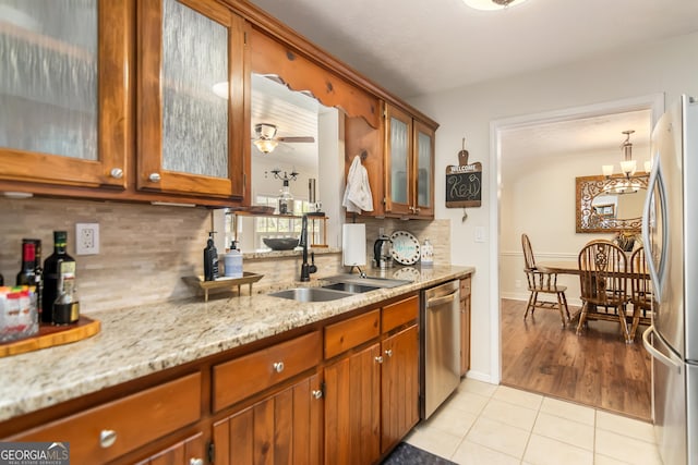 kitchen featuring light stone counters, light tile patterned floors, a sink, decorative backsplash, and appliances with stainless steel finishes