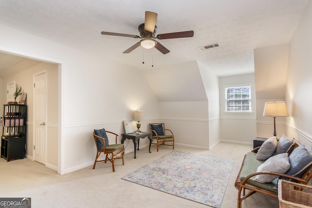 living area with visible vents, vaulted ceiling, carpet floors, a textured ceiling, and a ceiling fan