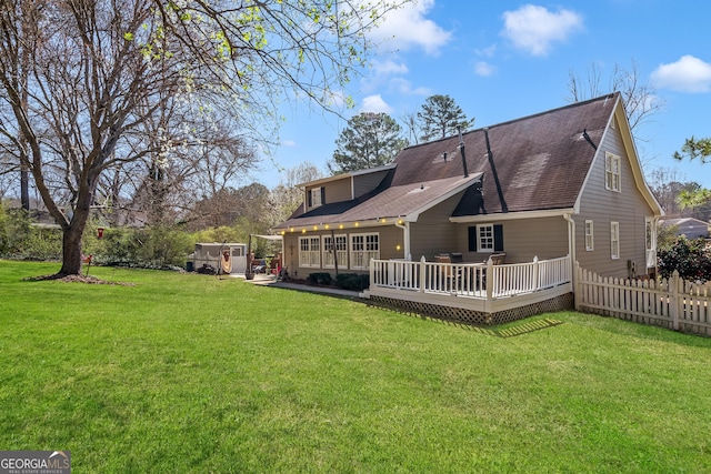 rear view of property with fence, a lawn, roof with shingles, and a wooden deck