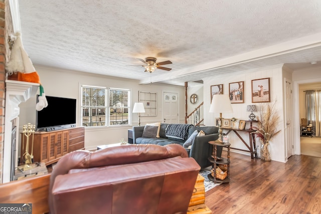 living area with a textured ceiling, wood finished floors, a brick fireplace, ceiling fan, and stairs