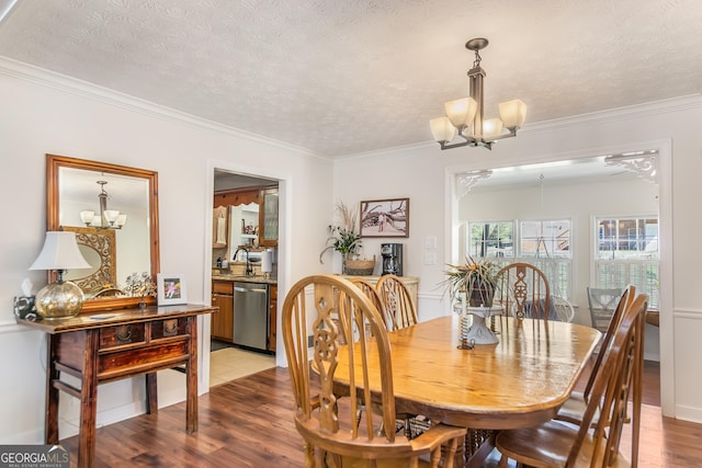 dining room featuring a textured ceiling, ornamental molding, light wood-type flooring, and a chandelier